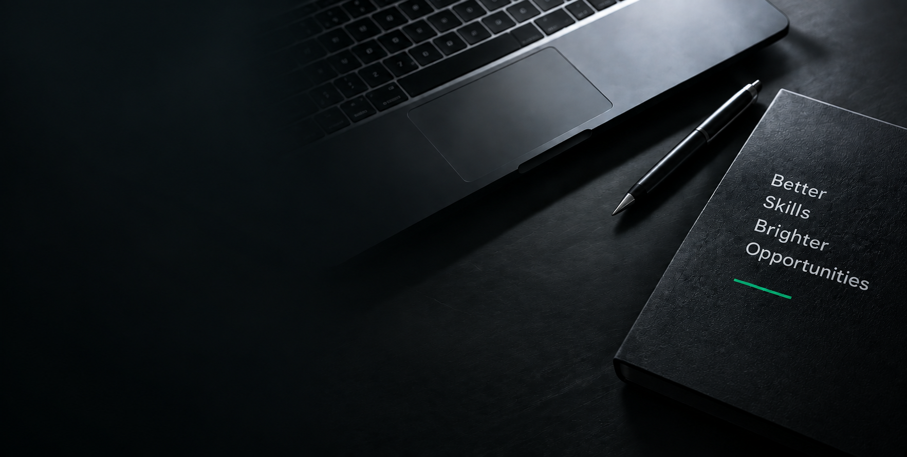 Dark desk with a laptop, pen and notebook